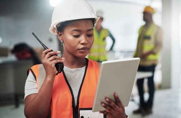 A construction working looking at a tablet while holding a radio.